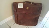 Closed front view of brown leather travel garment bag showing handle and leather trim