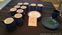Photo of 10 blue Denby coffee mugs along with 5 cream and blue rim dessert plates, plus one green/blue patterned mug and plate arranged on a table.