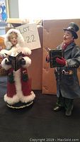 Photo showing both the male and female Abbott Christmas Carolers figurines, 10 inches high, in winter attire holding carol books.