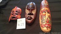 Three wooden masks with tribal designs and various color schemes displayed on a dark surface.