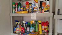 Overview of the cleaning supplies lot showing numerous spray bottles, aerosol cans, and cleaning cloths on two wall shelves.