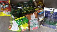 Overview photo of assorted garden product bags including potting soil, fertilizer and sand on concrete floor.