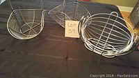 Three metal wire baskets arranged on a table, two have handles and one is on a stand