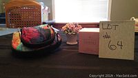 Overview photo of entire lot showing cosmetic bag, ceramic flower bouquet, and boxed perfume bottle on table.