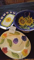 Three ceramic serving pieces: two platters and one bowl with floral designs placed on a black surface.