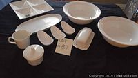 Overview of all white ceramic serving pieces on display including trays, bowls, creamer, butter dish, sugar bowl, and small dishes.