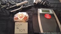 Two curling irons, a blow dryer, and a Weight Watchers electronic scale visible on black fabric surface with lot number card.