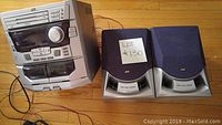Full shot of JVC MX-J10 stereo system with dual speakers on wooden floor showing overall system and speaker design.
