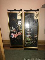 Pair of Asian wall plaques standing side-by-side, showing full front view with tags attached and black decorative hanger brackets on top and bottom.