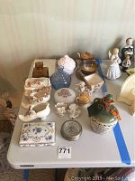 Photo showing full assortment of items on table including pottery bottle, figurines, china box, and glassware.