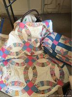 Photo showing Wedding Ring quilt with multicolor and pink/blue squares alongside folded blue star patterned quilt and basket in background