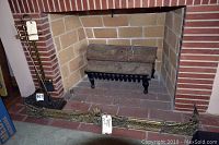Photo of fireplace showing brass fire screen, black metal log holder with artificial logs, and fireplace brick interior.