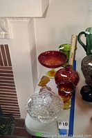 Photo showing amber and red Amberina glass items including a tall pedestal bowl, a covered candy dish, a Moon and Stars goblet, a small amber dish, and a clear cut glass serving bowl.