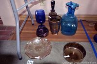 Full view of the six vintage glass items: two vases, one pitcher, one large scalloped bowl, one purple candy dish, and one amber bowl.