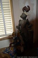 Wooden knight wall hanging standing behind the ceramic Foo Dog statue near window blinds, showing knight's detailed armor and feather plume on helmet