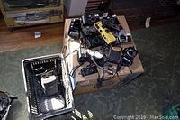 Top view showing a variety of cameras, some cameras with straps, and a few lenses, all positioned on a cardboard box on the floor.