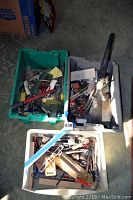 Three plastic containers filled with assorted hand tools and hardware items including measuring tapes, scissors, files, wrenches, and other workshop tools.