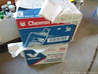 Photo showing two sealed cardboard boxes stacked, one labeled Chevron SAE 30 motor oil and the other unidentified but related to motor oil packaging.