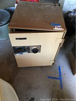 Front view of a beige Montgomery Ward safe with combination dial and handle, placed on concrete floor.