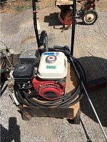 Top and front view of Honda pressure washer showing engine, hose coiled around base, and handle on a wheeled metal frame.