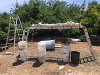 Photo showing an aluminum Versa multi-position ladder extended horizontally between several plastic buckets and a blue drum outdoors.