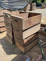 Stacked vintage wooden fruit boxes outdoors on dirt ground. Visible wear and varying wood shades.