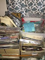Overview of various plastic bags filled with cross stitch and needlework patterns and materials packed in a box.