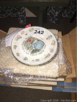 Stack of boxed and bubble wrapped collector plates with visible artwork showing Peter Rabbit and birthday greeting.