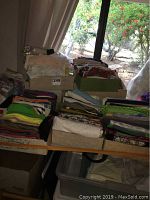 Table showing multiple boxes and trays filled with fabric remnants and full cuts of various sizes and colors, placed indoors by a window.