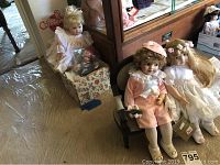 Four porcelain dolls displayed showing detailed clothing and facial features, seated next to doll sized love seat.
