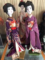 Three Japanese Geisha dolls posed together, showing size difference and detailed kimono patterns