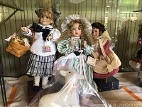 Three vintage nursery rhyme dolls displayed on stands: Little Bo Peep in green and white striped dress, companion dolls in plaid and red outfits, arranged on shelf with original boxes nearby.