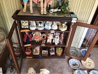 Front view of wooden display cabinet filled with collectible figurines, showing three shelves and glass door closed.