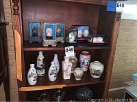 Shelf with nine Asian themed vases and several decorated painted eggs in display cases on upper shelf.
