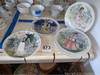 Overview of all eight Limoges decorative plates arranged on a table showing different vintage styled women in detailed dresses.
