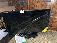 Black Sceptre 32-inch flat screen TV with remote and paperwork on floor.