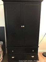 Front view of the modern black armoire showing two doors and two drawers with silver handles.