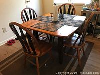 Wooden rectangular extendable dining table with 4 wooden chairs around it. Black legs on table base, medium brown wood finish.