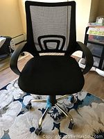 Front view of black office chair with mesh back and cushioned seat on a carpeted floor.