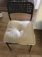 Front view of a black steel frame chair with perforated backrest and beige cushion on seat.