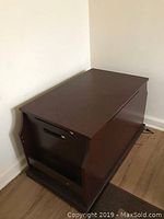 Photo of the brown wooden center table placed in a corner showing its side panel that provides access to the storage compartment.