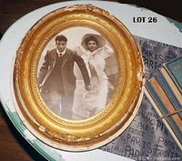 Front view of the sepia photograph of a couple inside the ornate gold oval frame on a wooden surface.