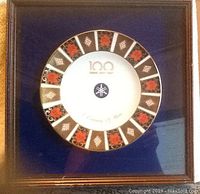 Square wood shadow box frame showing plate mounted on blue fabric background under glass. Frame has some damage and nicks.