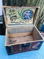 Open view of trunk showing vintage lithographed advertising paper on interior lid with floral and child image, and empty wooden interior.
