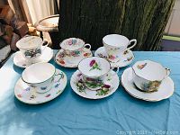 Photo showing all six sets of cups and saucers with different floral patterns on a blue cloth surface outdoors in natural light