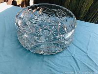 Side angle view of large heavy cut crystal bowl on blue cloth background, showing intricate geometric and fan cut designs.