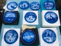 Top down view of 12 blue and white porcelain Christmas plates arranged on a flat surface showing various winter scenes.