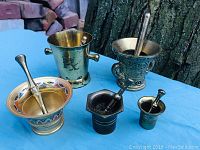 Full set of five brass miniature mortar and pestles on blue cloth, including various sizes and styles in brass with some patina.