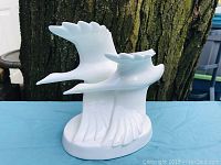 Front view of white fine bone china figurine depicting two seagulls flying over waves, set against a tree background.