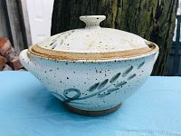 Side angle of vintage pottery serving casserole with lid, showing leaf design and speckled finish